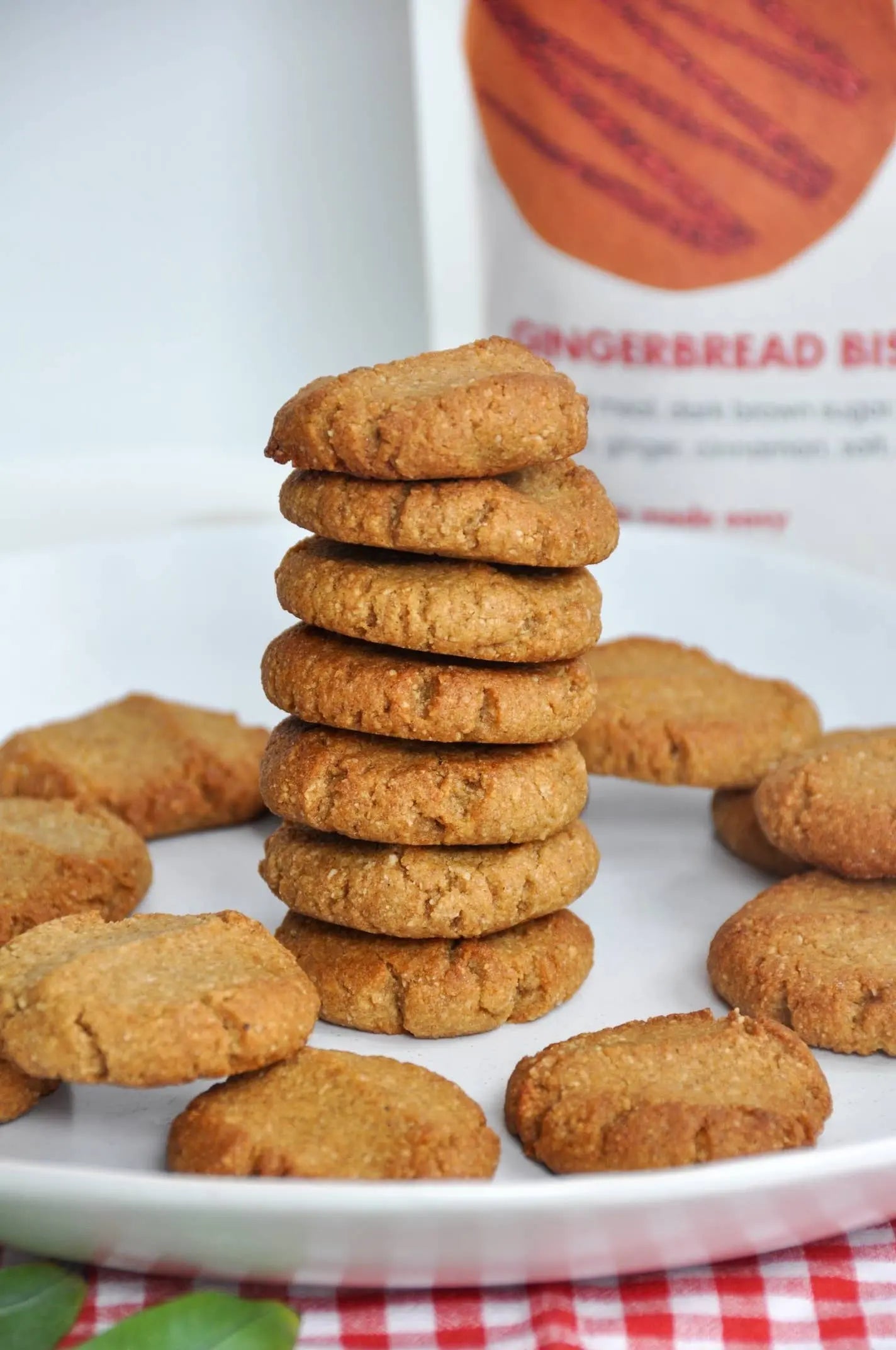 Stack of gingerbread cookies on a white plate with a gingerbread biscuit box in the background.