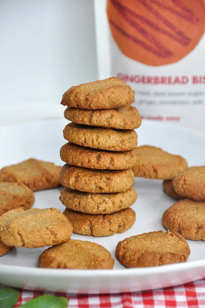 Stack of gingerbread cookies on a white plate with a gingerbread biscuit box in the background.