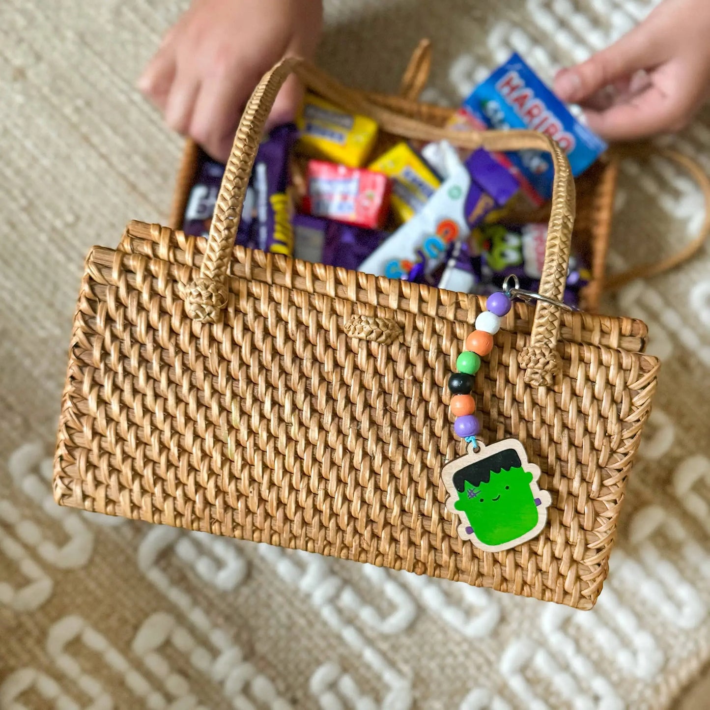 Woven handbag filled with colorful candy on a patterned surface and a monster diy Keyring 