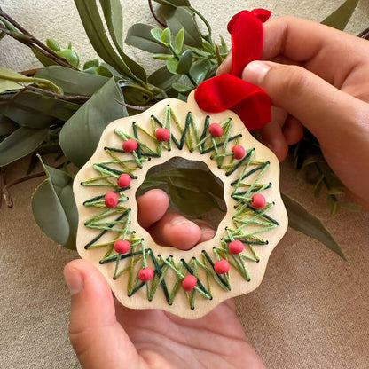 Handmade wooden ornament with greenery and red berries held by a person against a natural background.